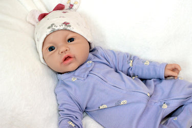 A baby doll resting on a soft white blanket, showcasing its delicate features and clothing.
